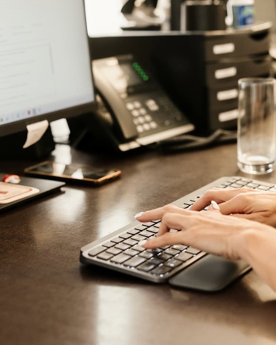 Mitarbeiterin am Schreibtisch tippt an der Tastatur, Monitor und Telefon daneben
