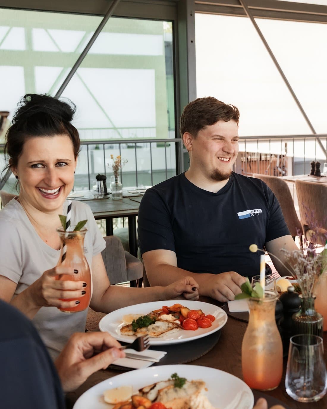 Zwei Kollegen lachen beim gemeinsamen Mittagessen auf der Gasthaus-Terrasse
